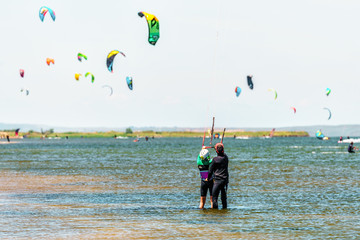 Kitesurfer trainer at sunny Black Sea Blaga Beach resort trains woman in kitesurfing standing in calm shallow waters of firth on distant flying kites background