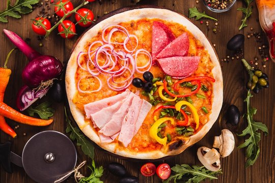 Italian Four Seasons Pizza (Pizza Quattro Stagioni)  on a dark wooden background with ingredients around (close  top view)