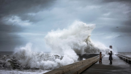 Crazy brave people on the pier near the lighthouse make photos during heavy storm against the...
