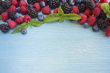 Various fresh summer berries on wooden background. Ripe blueberry, raspberry and blackberry with basil leaves. Berries at border of image with copy space for text. Top view.