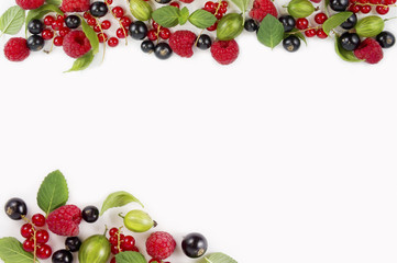 Various fresh summer berries on white background. Ripe raspberries, currants, gooseberries, mint and basil leaves. Berries at border of image with copy space for text. Background berries.