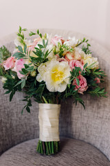 Bridal morning details. Wedding bouquet of yellow, beige and pink flowers with greenery on a chair.