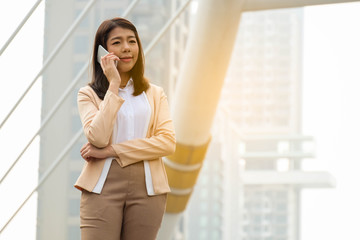 Portrait of beautiful young business woman standing in city, talking on the phone and smiling.