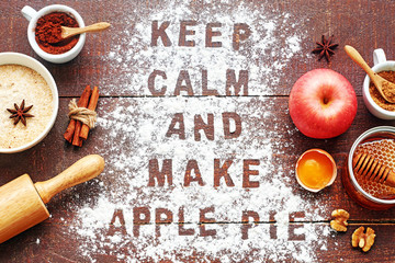 Making apple pie background. Apple pie ingredients with "keep calm and make apple pie" inscription. Roller pin, flour, apple, egg, honey, cocoa, sugar, walnut, spices on rustic table. 