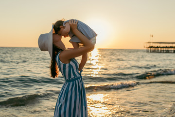 Beautiful young mother kiss daughter at the sea sunset and beach background. Happy family vacation. Travel. Caucasian happy female with baby outside at ocean sunset. Motherhood love care. Silhouette - Powered by Adobe