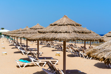 Beach straw umbrellas and sunbeds on the sandy sea shore. A bright sunny day. Clear blue sky.