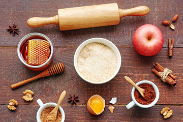 Baking ingredients for apple pie. Whole grain flour, egg, apple, sugar, honey, cocoa, cinnamon, almond, walnut, roller pin on a wooden table. 