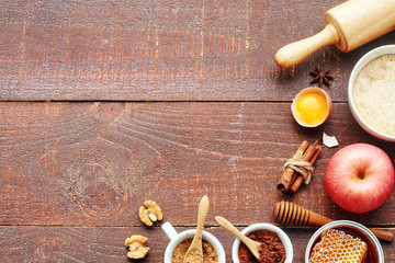 Baking ingredients for making apple cake. Fresh apple, flour, egg, honey, walnut, cinnamon, cocoa powder, brown sugar, roller pin over rustic wooden table. Copy space.
