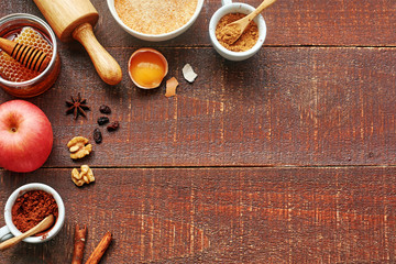 Baking ingredients for making apple cake. Fresh apple, flour, egg, cocoa powder, cinnamon, honey, walnut, raisins, roller pin on rustic wooden background. Copy space, top view.