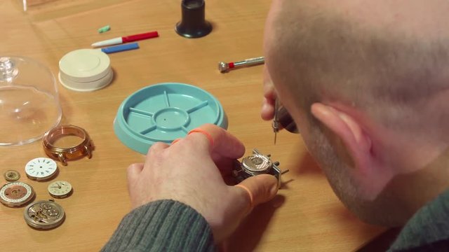 Bald male clockmaker disassembling some mechanical clock. Close up of mature man unscrewing the screw from the clock mechanism. Caucasian watch repairer using tweezers at his work