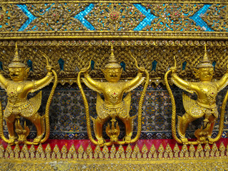 Fototapeta na wymiar Golden garuda holding naga statue fully front view with ornamental decoration on temple wall