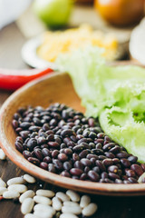 Black beans on brown pottery plate over wooden board.