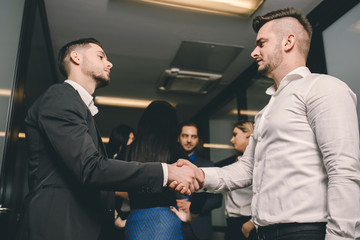 Two business men handshaking with their team behind them