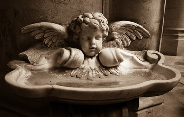 Baby angel over holy water stoup in church. Sepia.