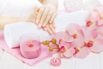 Fototapeta na wymiar beautiful pink manicure with orchid, candle and towel on the white wooden table.