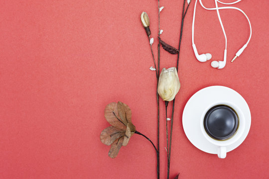 White coffee cup with paper flower and earphone on red paper background.