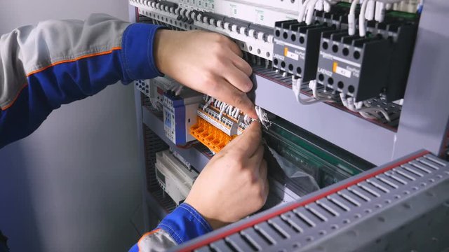 Electrician installing wires, cables into a electricity power shield, fuse box. 4K.