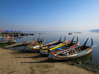 Colorful wooden boats on bank of peaceful still water lake with port, birds and clear blue sky background