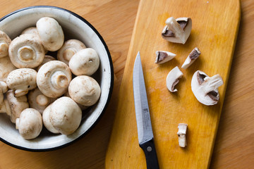 Raw champignon mushrooms in white bowl on wooden table background
