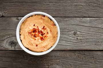 Bowl of spicy hummus, above view over a rustic wood background
