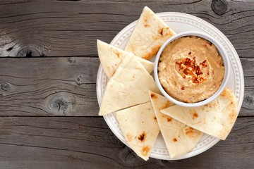 Hummus dip with pita bread on a plate, above view on a rustic wooden background - obrazy, fototapety, plakaty
