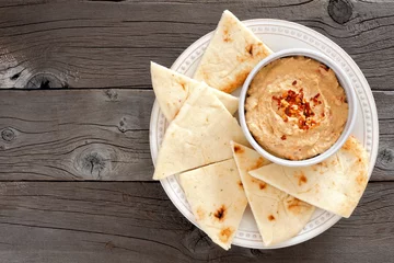 Wandaufkleber Hummus dip with pita bread on a plate, above view on a rustic wooden background © Jenifoto