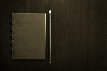 Black blank notebook with pencil on dark chalkboard background.