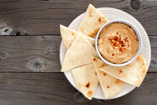 Fototapeta Hummus dip with pita bread on a plate, above view on a rustic wooden background