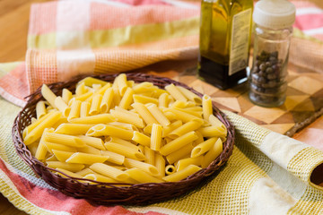 Raw penne pasta with olive oil and pepper on wooden table