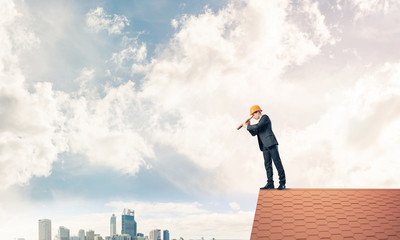 Engineer man standing on roof and looking in spyglass. Mixed med