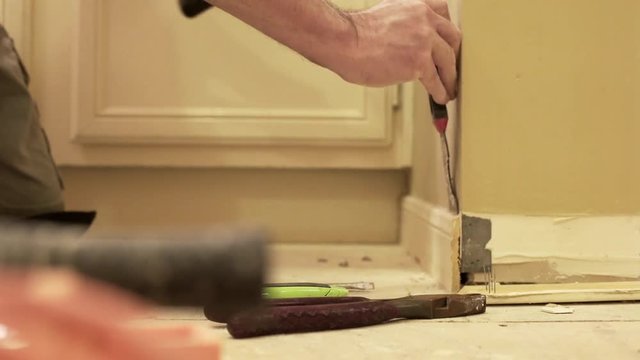 A laborer or homeowner handyman type removing old baseboards from the wall.