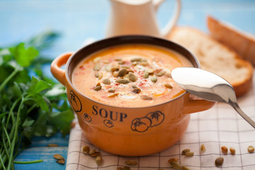 Homemade pumpkin soup with cream, bread, greens and pumpkin seeds on a wooden background. Top viev