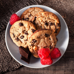 Chocolate chip cookies on white plate dark old wooden table with red raspberry and  place for text.,  freshly baked. Selective Focus with Copy space..