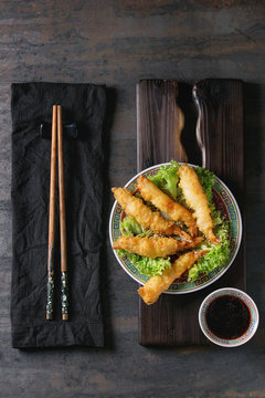 Fried tempura shrimps on lettuce salad with sauce. Served in traditional china plate with chopsticks on wood serving board and textile napkin over old metal background. Top view, space. Asian dinner
