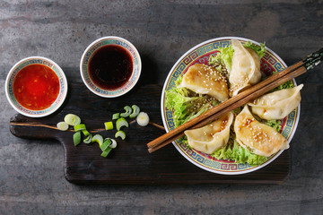 Gyozas potstickers on lettuce salad with sauces. Served in traditional china plate with chopsticks and black teapot on wood serving board over old metal background. Top view, space. Asian dinner