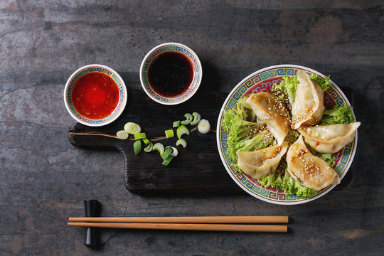 Gyozas potstickers on lettuce salad with sauces. Served in traditional china plate with chopsticks and spring onion on wood serving board over old metal background. Top view, space. Asian dinner