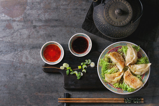 Gyozas potstickers on lettuce salad with sauces. Served in traditional china plate with chopsticks and black teapot on wood serving board over old metal background. Top view, space. Asian dinner