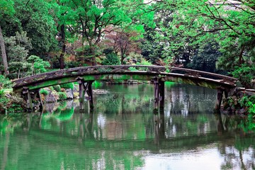 Fototapeta na wymiar Scenery of a beautiful Japanese garden in Shosei-en of Higashihonganji Temple in Kyoto Japan, with view of a wooden bridge over the lake and forests of refreshing greenery reflecting on peaceful water