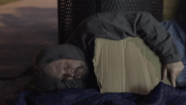 Sleeping homeless man awakes to someone giving him money.
