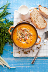 Homemade pumpkin soup with cream, bread, greens and pumpkin seeds on a wooden background. Top viev