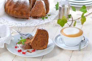 Schoko-Guglhupf mit  Zartbitterschokolade mit einer Tasse Cappuccino serviert - Freshly baked ring-shaped cake with chocolate, so called Gugelhupf in Austria and Germany, served with a cup of coffee