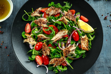 Smoked Mackerel Salad with tomato, chopped red onion, Ruccola on black plate.