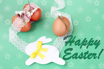 easter hand made decorated greeting card: easter eggs with white lace and festive paper bunny isolated on green background with inscription happy easter