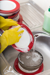 Cleaning dishware kitchen sink sponge washing dish. Close up of female hands in yellow protective rubber gloves washing