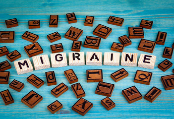 migraine word written on wood block. Wooden alphabet on a blue background.