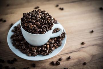 coffee cup filled by coffee beans on wooden background