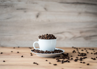 coffee cup filled by coffee beans on wooden background
