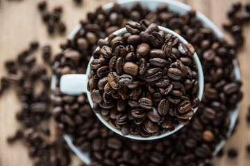 coffee cup filled by coffee beans on wooden background