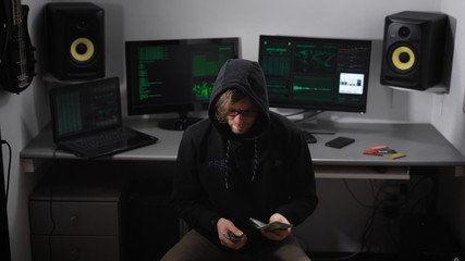 Hooded hacker in black clothes sitting on a chair in the room and counting prepayment for hacking...
