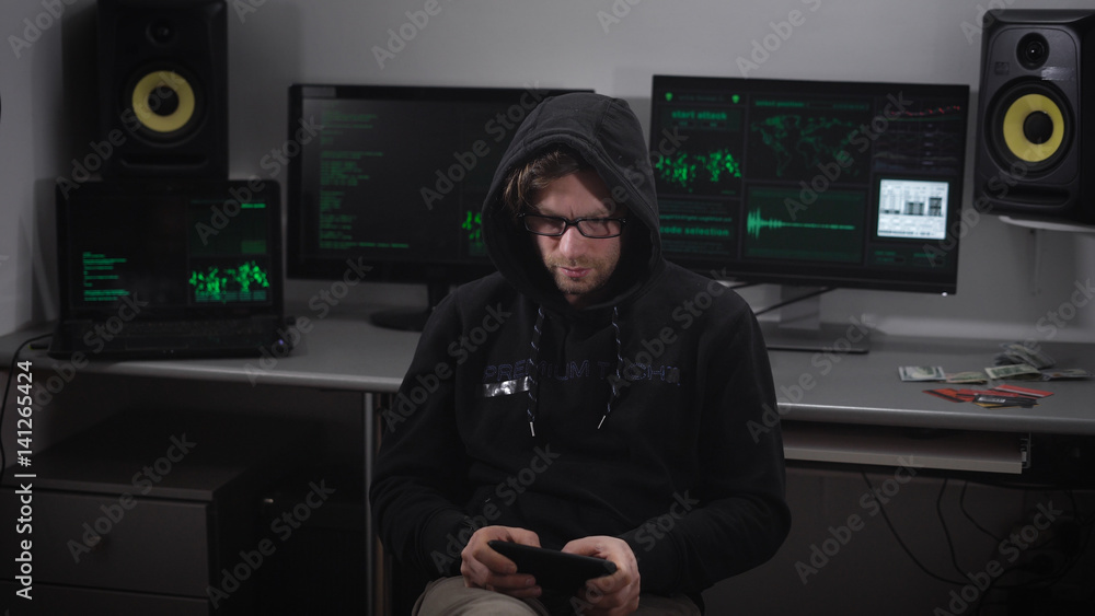 Poster close up of hooded hacker making cyberattack on network with the help of tablet in his hands. man is